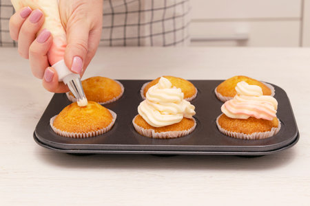 Woman hands decorated with cream tray with freshly made cupcakes or maffins on wood table at the...
