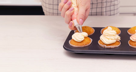 Woman hands decorated with cream tray with freshly made cupcakes or maffins on wood table at the...