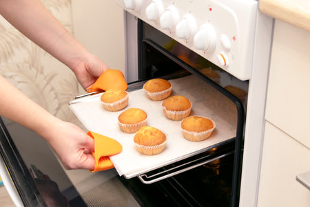 Caucasain woman holding tray with freshly made cupcakes or maffins at the kitchenの写真素材