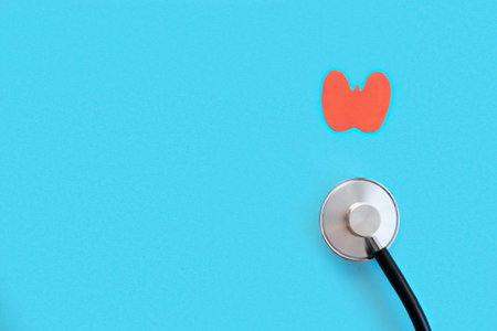 Paper model of healthy thyroid and stethoscope on light blue background, flat lay with copy space...