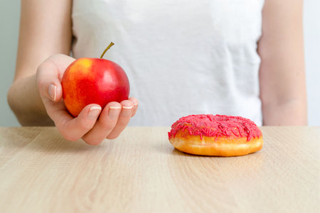 a woman holds an apple and a donut in her hands. concept of choosing healthy food and unhealthy foodの写真素材