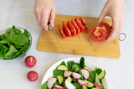 Woman hands cooking fresh healthy organic salad of spinach, cucumber, tomato and radish in white...