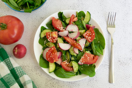 Raw fresh green healthy organic salad of spinach, cucumber, tomato and radish in white bowl on table top view on grey background.の写真素材