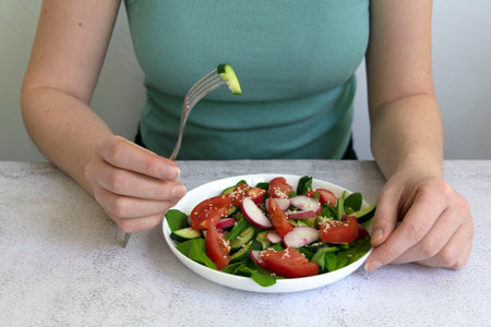 Woman hands cooking fresh healthy organic salad of spinach, cucumber, tomato and radish in white bowl on table top view on grey background.の写真素材