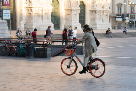 Milan, Italy - May 4, 2020: Woman riding bicycle through Duomo square. Italy enters second phase of coronavirus COVID-19 lockdown. People wearing face mask and maintain social distancingのeditorial素材