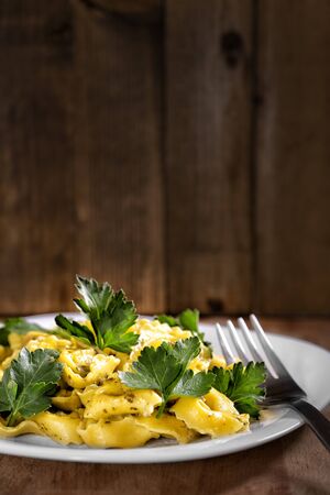 Ravioli with fresh parsley leaves on wooden rustic surface. Traditional italian kitchen cuisine. Cooked ravioli pasta in dish under creamy sauce on concrete brown table. Macroの写真素材