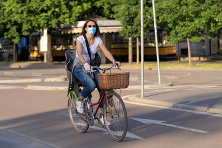 Milan, Italy - May 8, 2020: Woman exercising on bicycle outdoor wearing medical mask. Outdoor sport practice during coronavirus outbreak period. New normal. Second phase of quarantine in Europe.のeditorial素材