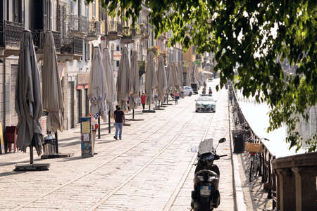 Milan, Italy - May 8, 2020: People walk in Naviglio Grande canal street wearing face mask. Police car keeps order. Second phase of quarantine in Europe. Concept of lockdown, flatten the curveのeditorial素材