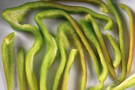 Green bell pepper slice or section texture. Creative pepper pieces layout. Set of sliced vegetables on white plate. Food art. Abstract minimal compositionの写真素材