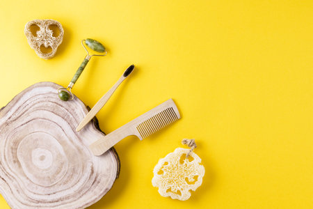 Eco beauty concept. Jade face roller, loofah sponges, toothbrush, wooden comb, wood slice on yellow surface. Set of items for beauty from ecological material. Zero waste for bath. Copy space, flat layの写真素材