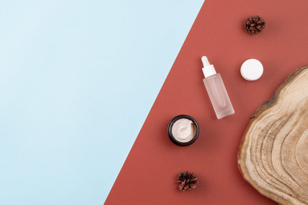 Skin care products. Open cream jar, serum with peptides, wooden cross section cut, pine cones on...