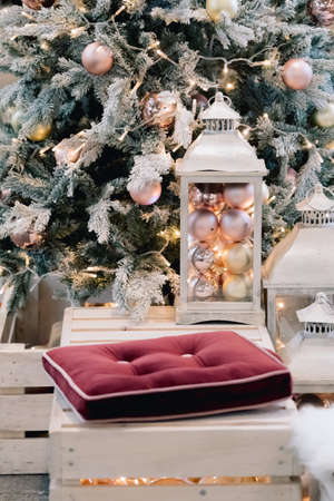 Lantern with holiday baubles on decorated christmas tree background in living room interior. Winter time and lamp on wooden sofa near christmas tree. Cozy vintage holiday interior. Selective focusの写真素材