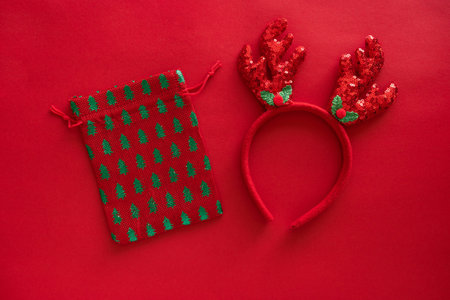 Christmas accessories, deer antlers headband on red glitter surface and gift bag, greeting card....