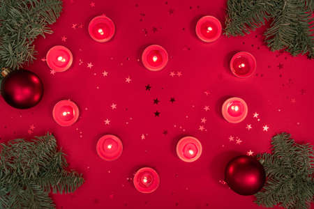 Christmas romantic evening composition made from burning candles, tree branches, glitter and baubles on red surface. Merry christmas and happy 2021 New Year concept. Flatlay, top viewの写真素材