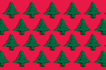 Christmas decorative trees on red surface. Object pattern of holiday felt tree with shadow. Trendy christmas wallpaper. Happy Holidays greeting card, banner.の写真素材