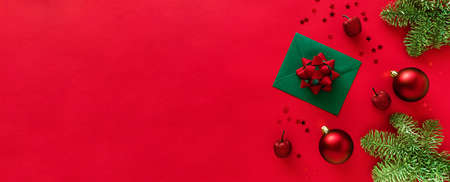 Christmas letter with greeting card and congratulations, christmas tree branches, baubles, decorations on red surface. Merry Christmas happy New Year concept. Flat lay from above, copy space, bannerの写真素材