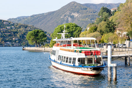 Como, Italy - October, 2019: Conventional ferry Innominato stopped at the dock in Como city. Public motor ship arrived or departing from station on Como lake. Tourists boat on sunny summer dayのeditorial素材