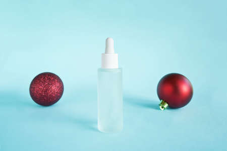 Serum oil with collagen and peptide in white transparent bottle with dropper on blue backdrop and red baubles. Skincare beauty treatment medical skincare mockup packaging liquid cosmetic productの写真素材