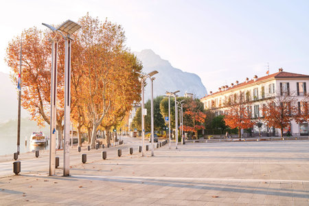 Sunny lakeside promenade of the Italian lakeside at famous lake Como. Embankment with alley and city square on sunny autumn day near lake with mountains on background. Lecco, Italy - November 08, 2020のeditorial素材