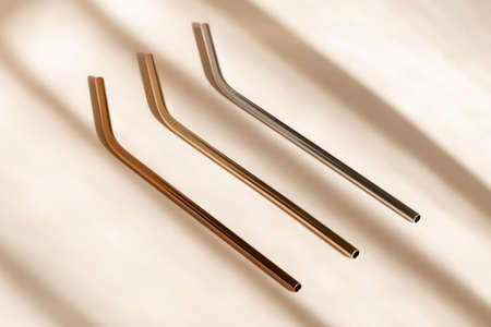 Reusable zero waste metal straw, eco friendly drinking straws from aluminium or stainless steel on neutral beige background with shadow from room windows, high angle view. Sustainability conceptの写真素材
