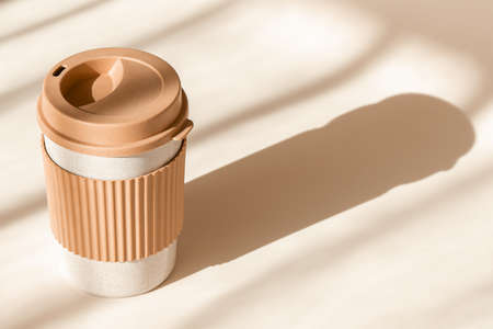 Reusable cup, biodegradable travel plastic coffee mug for take away. Sustainable bamboo eco friendly cup on natural shadow beige background. Zero waste, sustainability concept. Ban single use plasticの写真素材