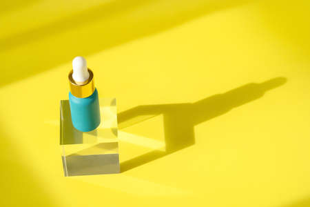 Hyaluronic acid skincare bottle on transparent crystall block podium pedestal. Cosmetics serum product with peptide and collagen. Modern packaging with shadows on yellow surface. Cosmetic showcaseの写真素材