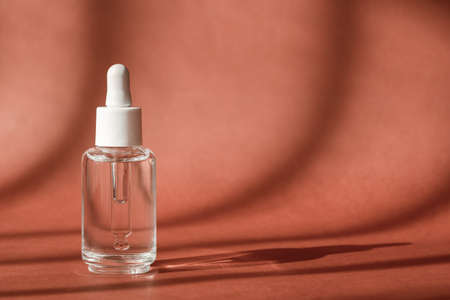 Serum cosmetic bottle, hyaluronic acid on brown background. Serum product cosmetic with peptide and collagen, modern brand glass cosmetics packaging. Showcase, art deco, natural shadowsの写真素材