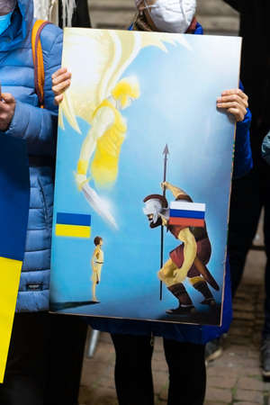 The poster with ancient warrior and russian flag on him against small man with ukranian flag under defence of an angel with a sword. Metaforic rappresentation of russian ukranian conflictのeditorial素材