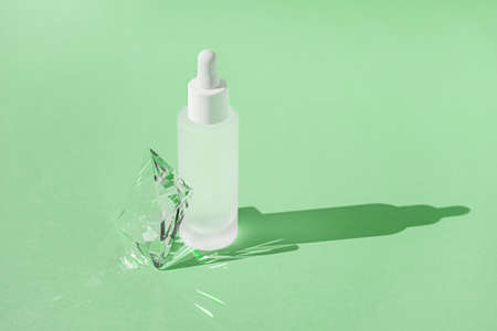 Serum skincare product with collagen and peptide in white bottle with dropper on green backdrop with crystal glass prism refracting light effects and rays of light. Product mockup packaging, bannerの写真素材