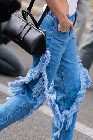 Milan, Italy - September, 21, 2022: woman wearing blue denim fringed pants and black leather Sunday bag from The Attico, street style outfit details.のeditorial素材