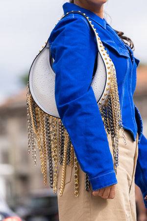 Milan, Italy - September, 21, 2022: woman wear blue denim asymmetric cropped long sleeves jacket, leather shoulder bag with nailed studded fringed chain pendant shoulder, street style outfit details.のeditorial素材