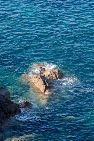 Wild rocky beach coastline and the sea, wave splashes on rock in sea shore, calm sea. Breaking waves to the rocks on shore creating white sea foam and small bubbles, top viewの写真素材