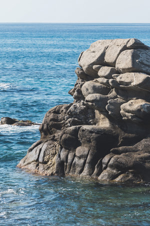 Wild rocky beach coastline and the sea, wave splashes on rock in sea shore, calm sea. Breaking waves to the rocks on shore creating white sea foam and small bubblesの写真素材