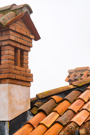Fragment of old weathered ceramic red tile roof, chimney on the building, roofing material
