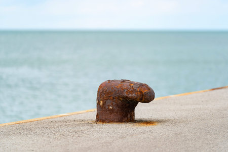 close-up of a rusted bollard on a concrete pier with the sea in the background