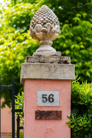 pink pillar with a decorative finial and house number 56, set against a lush green background