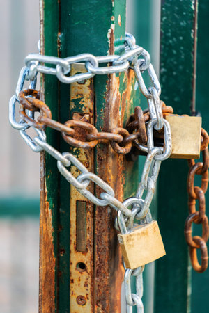 close up of padlock and chains wrapped around rusty gate with weathered paint