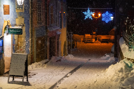 snow-covered street at night with festive lights and restaurant sign, creating a cozy winter sceneの写真素材