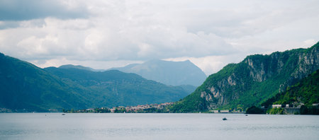 scenic view of lake surrounded by mountains and village in the distance under cloudy sky