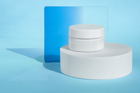 White cosmetic jar on blue background with abstract shadowsの写真素材