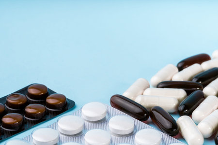 Close-up of various pills and capsules in blister packs and loose on a light blue background,...