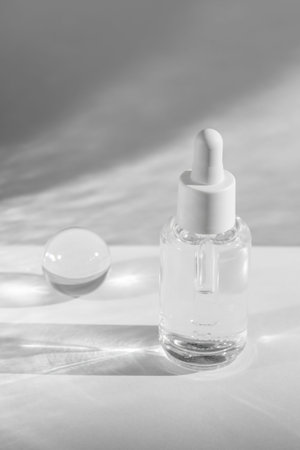 clear serum bottle and crystal ball creating elegant shadows on a white background, cosmetic showcaseの写真素材