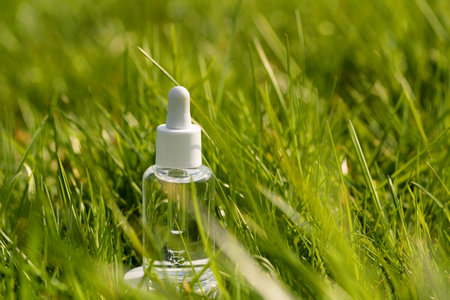 clear serum bottle lying in lush green grass, sunlight reflecting on the bottleの写真素材