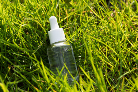 clear serum bottle lying in lush green grass, sunlight reflecting on the bottleの写真素材