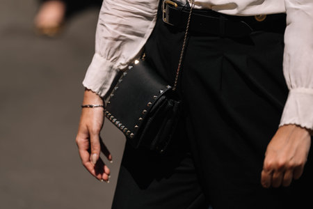 Milan, Italy - June, 16, 2023: Fashion detail shot of black handbag adorned with metal studs, held...