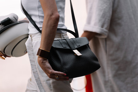 Milan, Italy - June, 19, 2023: close up of woman holding elegant black textured handbag, matched with white and grey attire. image emphasizes sophistication and sleek designのeditorial素材
