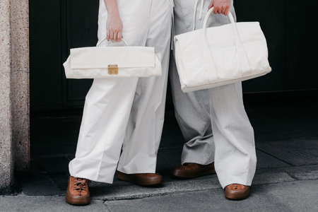 Milan, Italy - June, 25, 2022: two individuals holding minimalist white fabric bags, standing...