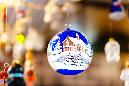 Blue Christmas bauble with detailed painting of snowy church and trees hanging in market stall. The hand-painted ornament captures the traditional beauty of the winter seasonの写真素材