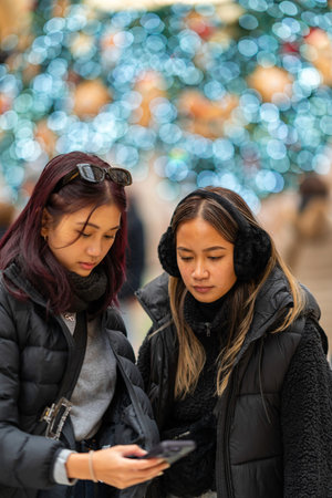 Milan, Italy - 18.12.2022: Two women dressed in warm winter jackets and earmuffs stand together,...