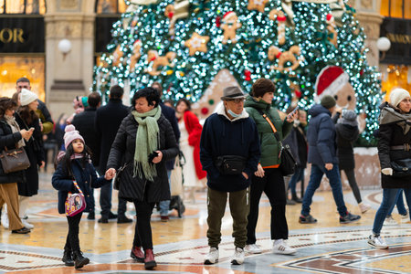 Milan, Italy - 18.12.2022: Families stroll around large, decorated Christmas tree adorned with lights and gingerbread ornaments. Festive atmosphere, holiday season in Gallery of Victor Emmanuelのeditorial素材